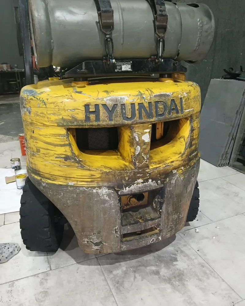 Traseira de empilhadeira Hyundai amarela desgastada, com pintura descascada e ferrugem, antes da reforma